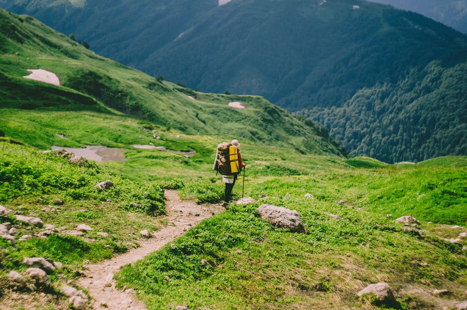 A hiker with a large backpack walking along a green mountain trail in summer, embracing adventure and nature.